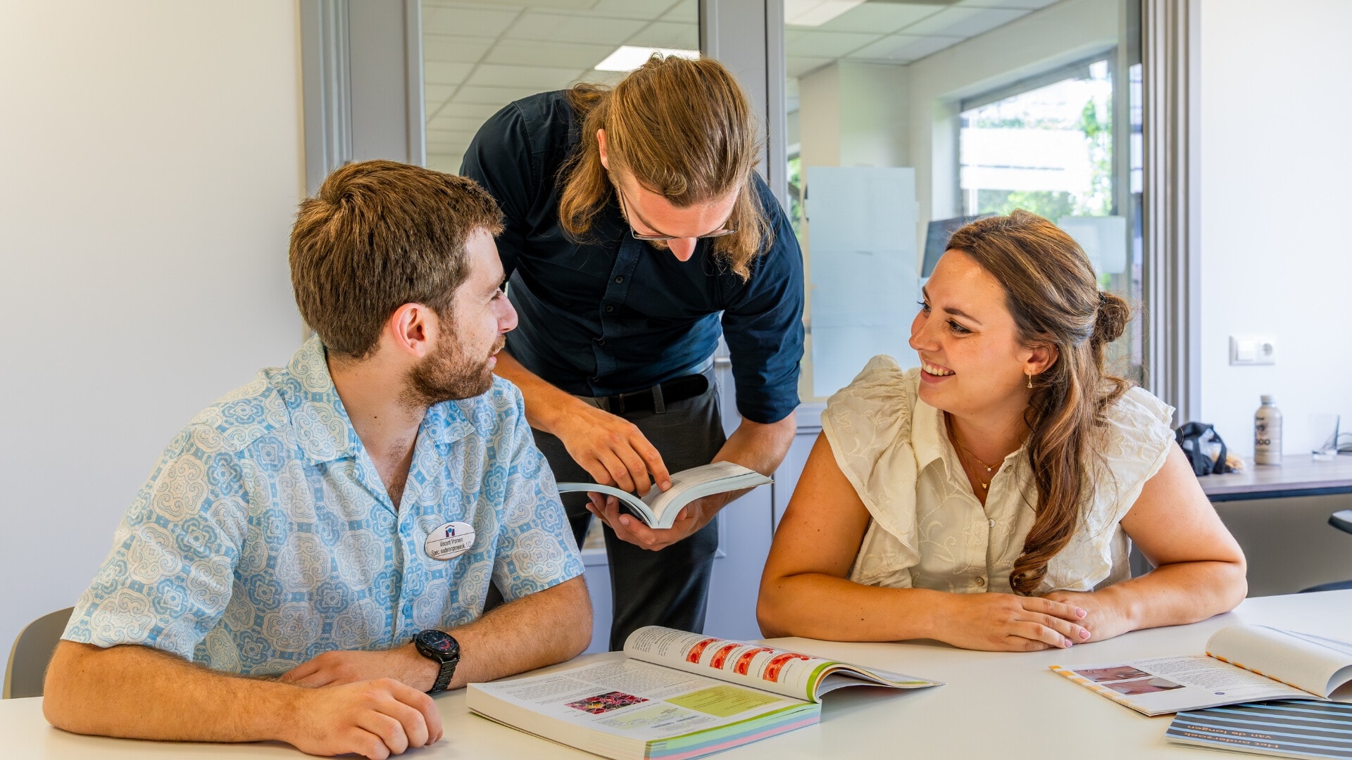 Drie studenten lachen en bestuderen lesboeken.