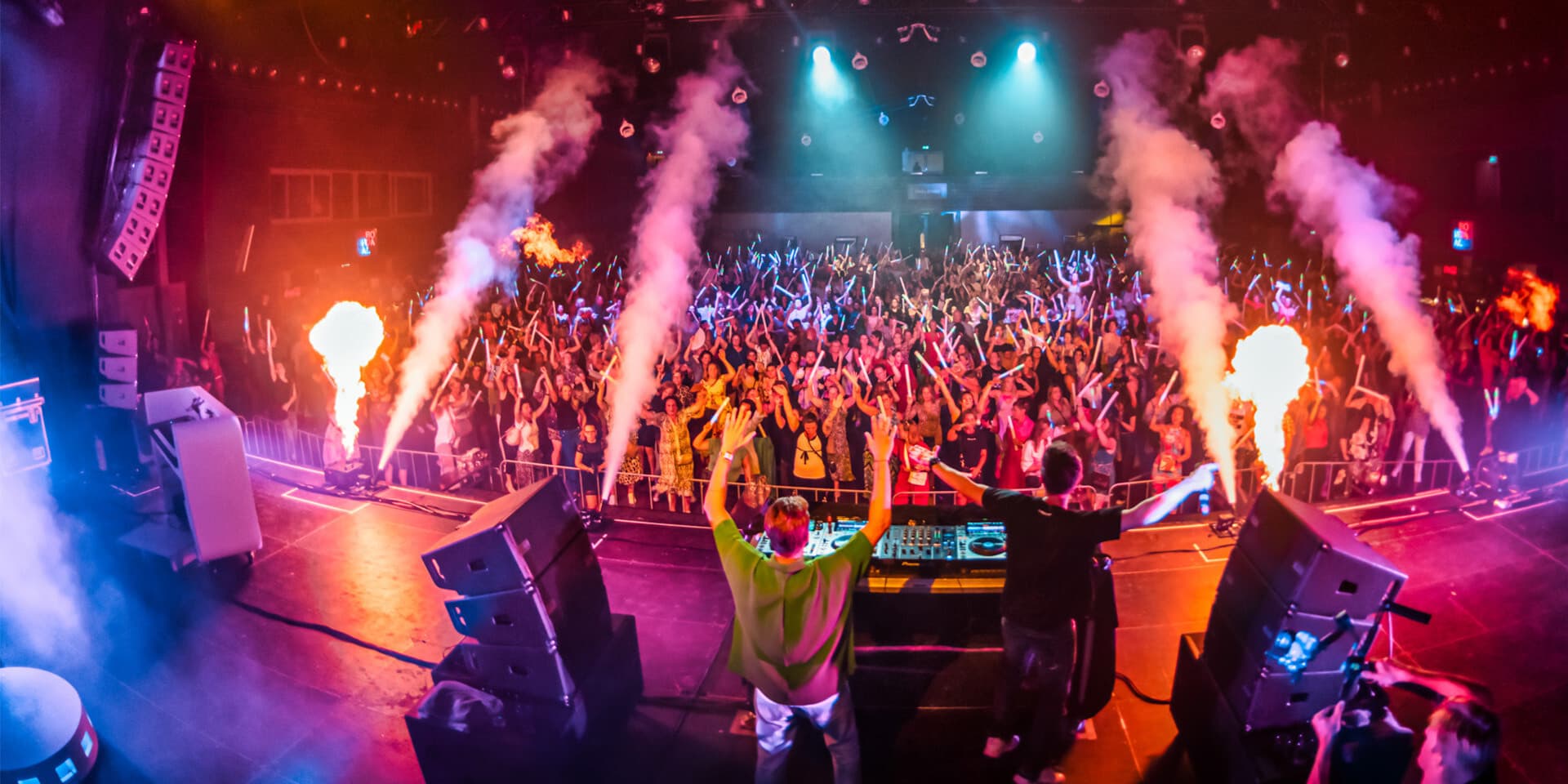 Een DJ draait muziek voor een juichende menigte op het Meander feest, met vlammen en rook als special effects.